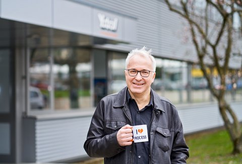 Hans-Joachim Jacob stands in front of a building and holds a cup in his hand